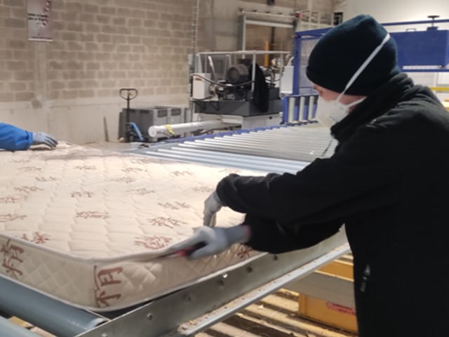 Two people in a workshop separating the textile envelope of the mattress from the foam block