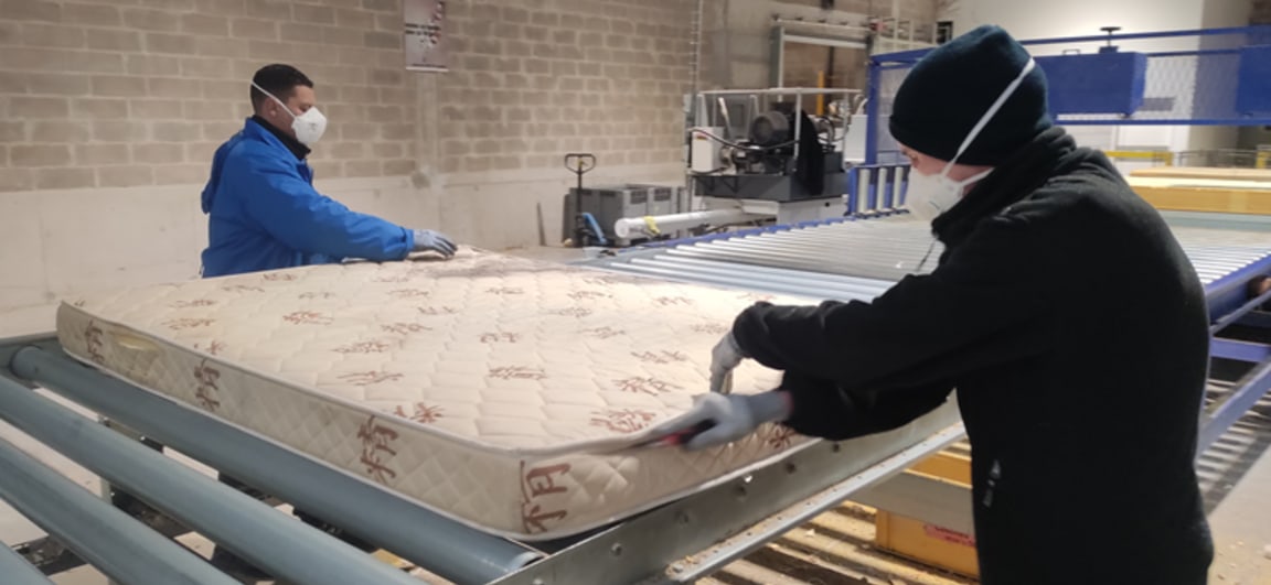 Two people in a workshop separating the textile envelope of the mattress from the foam block