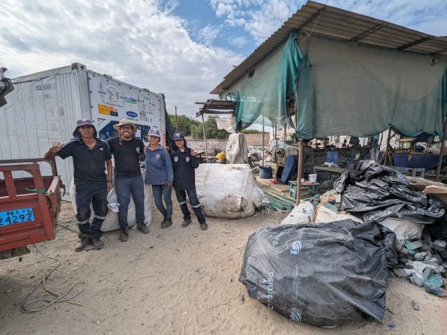 Four people stand outdoors at a plastic recylcing depot