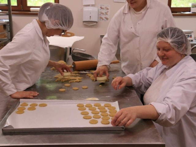 Three people in a commercial kitchen baking biscuits and cookies.